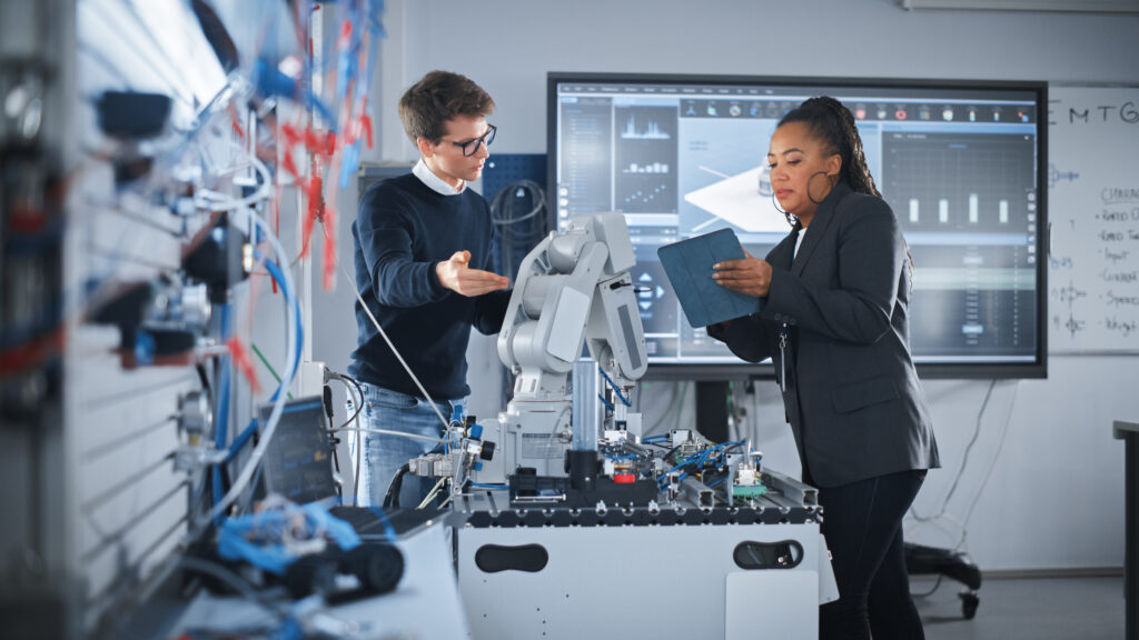 Black Teacher Holding Tablet and Discussing Robot Hand with Caucasian Student During the Lesson at School Computer Science Education, Design, Learning Concept Slow Motion